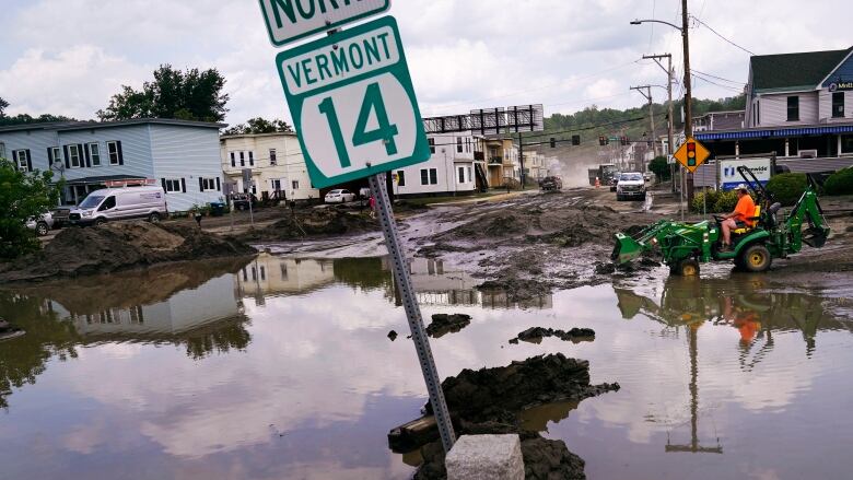 A small tractor clears water from a business as flood waters block a street