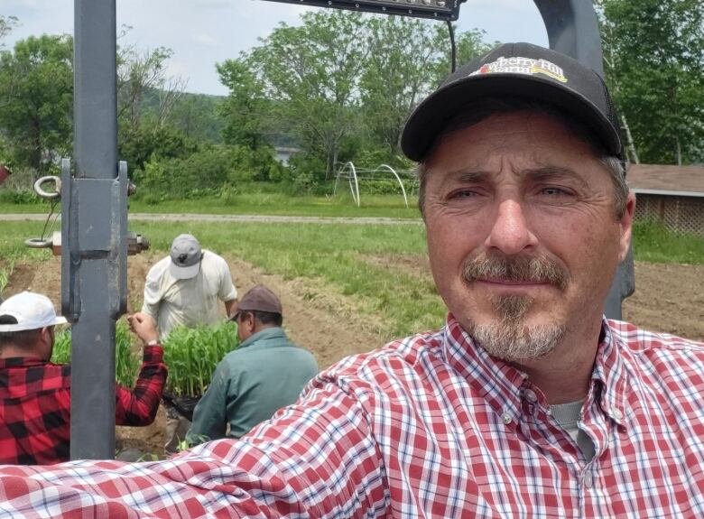 A selfie of a man on a tractor with people behind him tending to crops