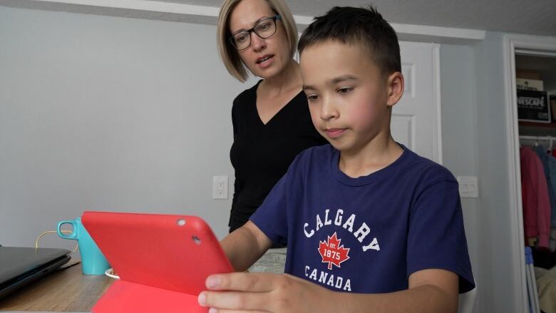 A lady in a black top is seen next to a boy wearing a blue T-shirt who's gazing intently at a device.