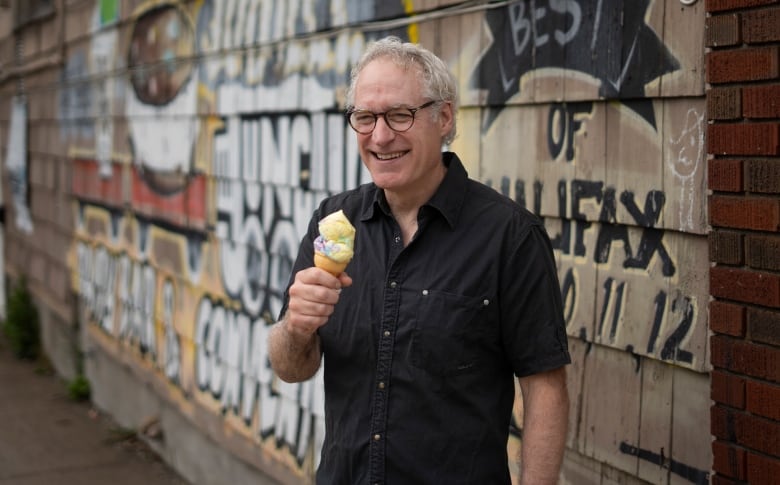 A man wearing a black short-sleeved shirt smiles while holding a Moon Mist ice cream cone.