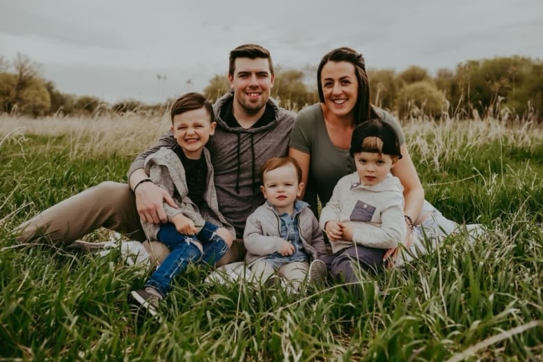 A family of five, including three young sons, sits in a field of long grass, posing for a photo.