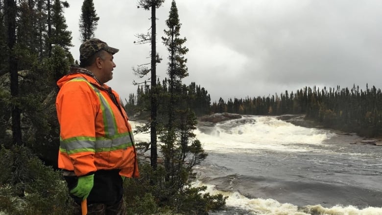 A man looks out over a tumultuous river.