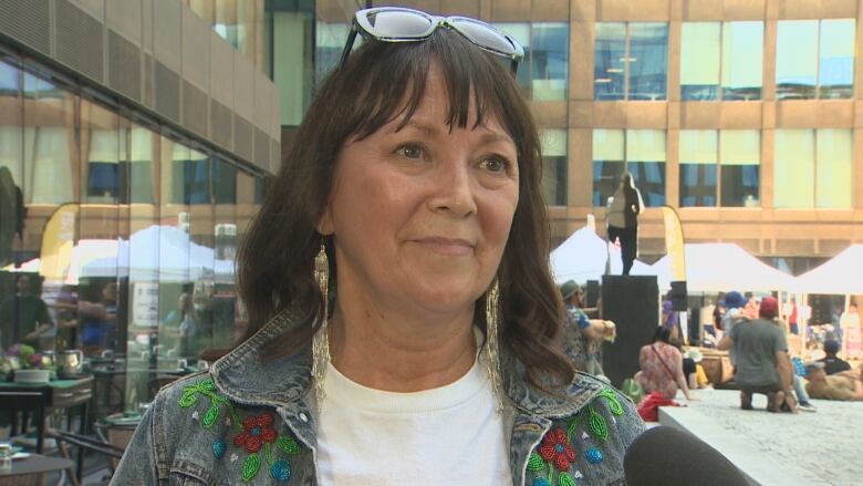 A woman in a denim jacket with floral embroidery speaks to the camera.