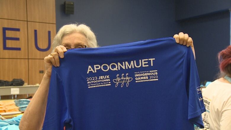 A volunteer holds up a blue NAIG volunteer shirt. On the back, it says 