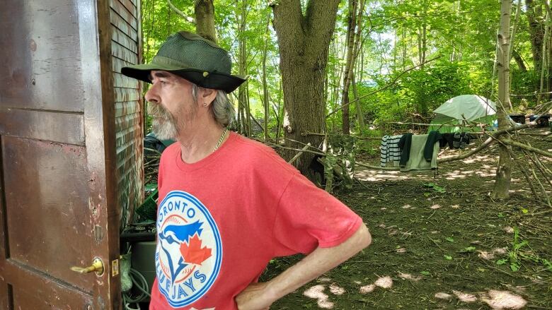 A man is shown wearing a green floppy hat and red Toronto Bluejays t-shirt with tents in the background.