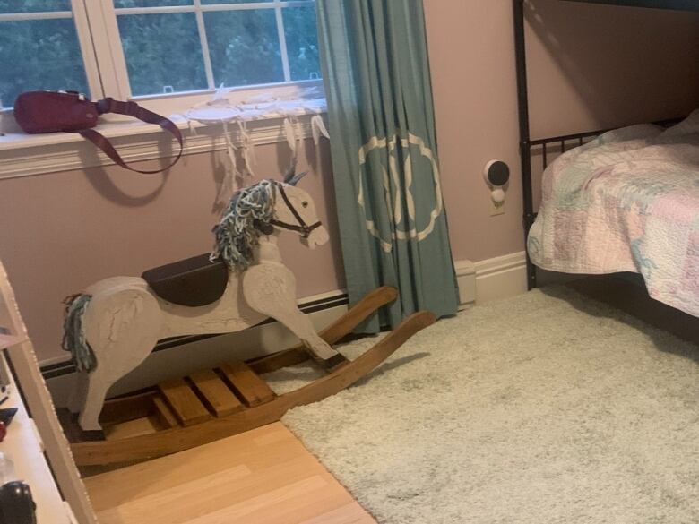 A wooden rocking horse sits in the corner of a bedroom.