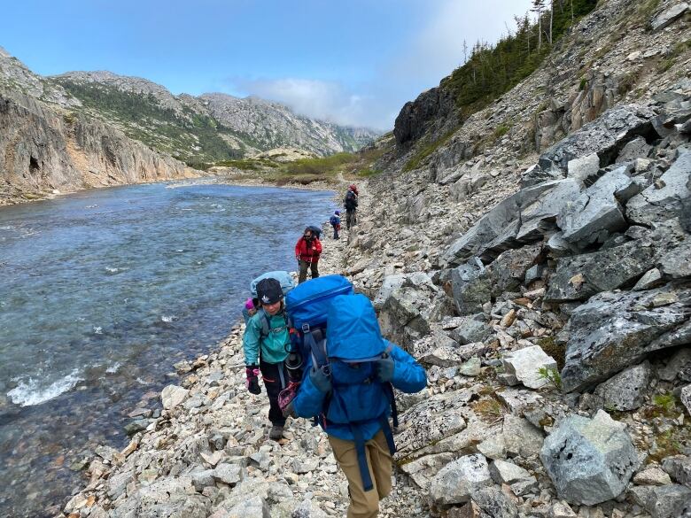 Hikers are seen walking beside a mountain creek.