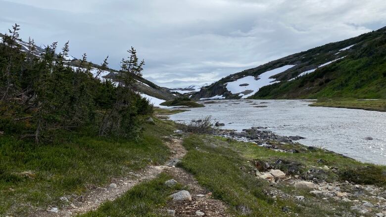 A trail is seen alongside a river in the alpine.