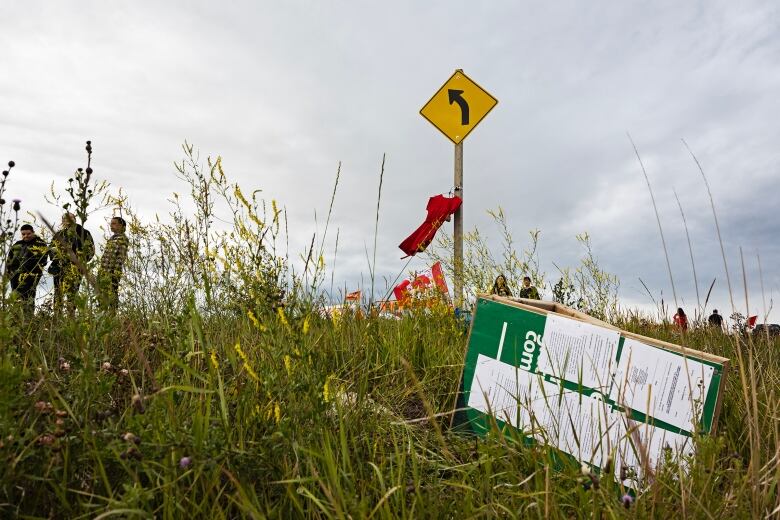 A sign with documents attached to it sits on its side in a ditch. A red dress hanging from a post blows in the wind in the background.