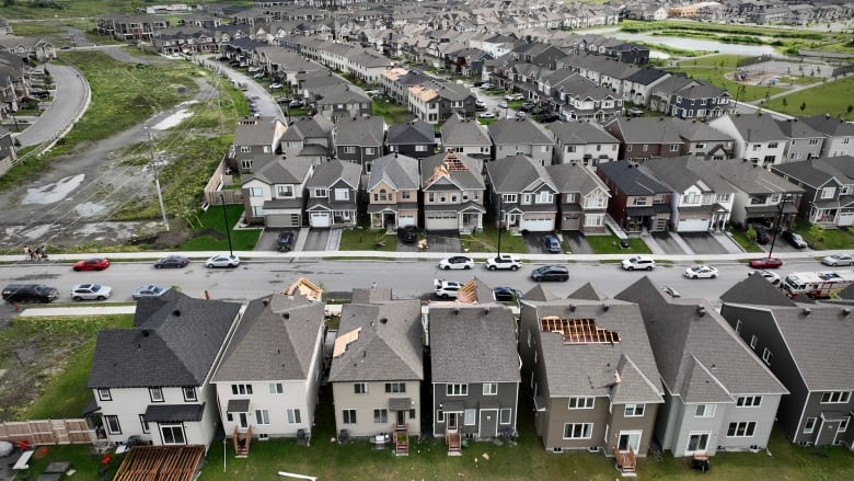 An aerial shot of a suburban housing development, with debris strewn about and damage to several roofs.