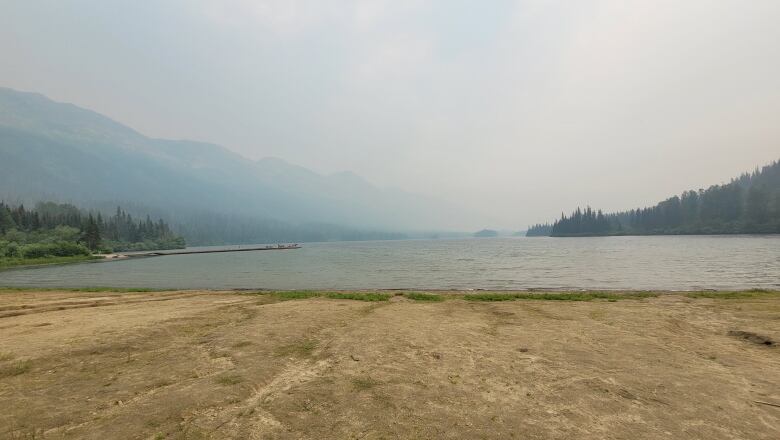 A horizon of mountains, water and a shoreline are seen clouded by smoke.