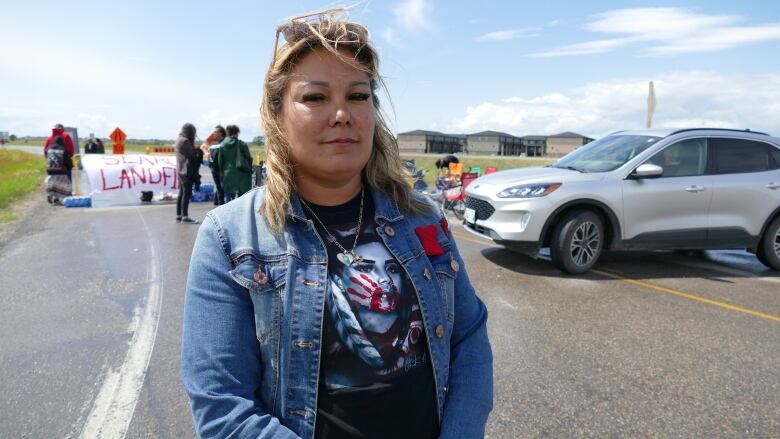 A woman stands on a road with a sign in the background that says 