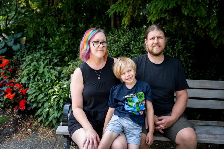 A woman with multicoloured hair and a brown-haired man sit on a bench, with a blonde boy between them.