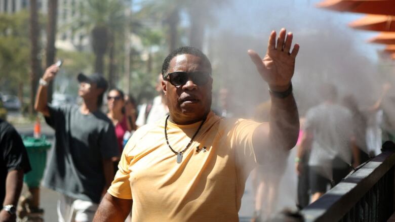 A man raises his hand to cool off near a municipal water mister in Las Vegas.