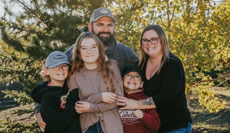 A white family of five stands in a group hug for a photo in a forested park.