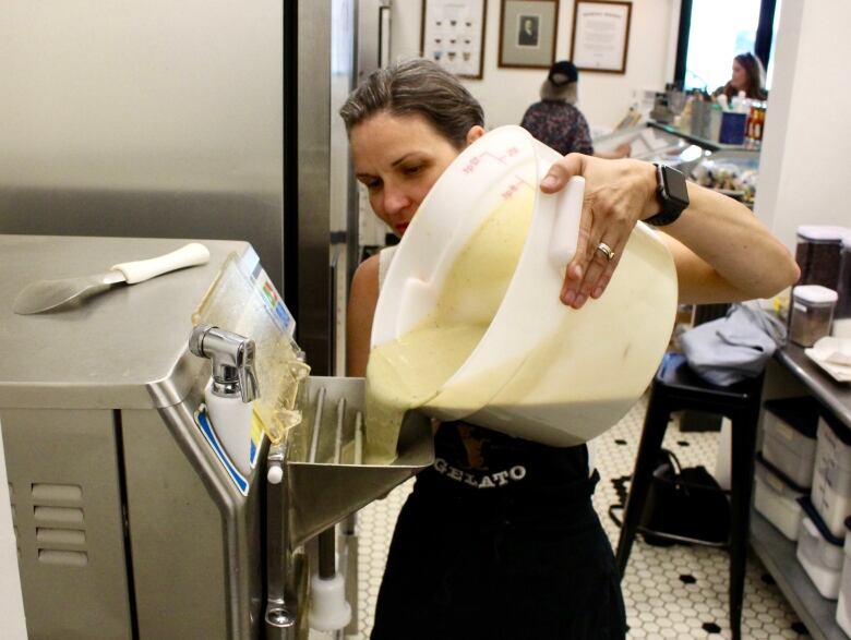 A woman pours a large bucket of a thick milk and sugar mixture into a metal machine.