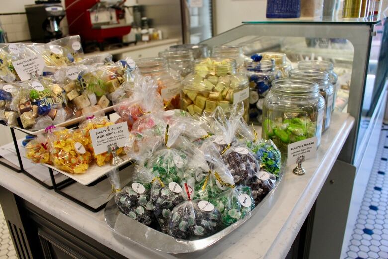 A counter in a store is packed with an assortment of colourful wrapped candies in little baggies and glass jars.