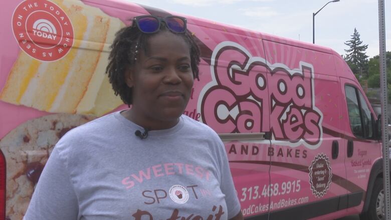 A woman poses in front of a pink van with a logo. 