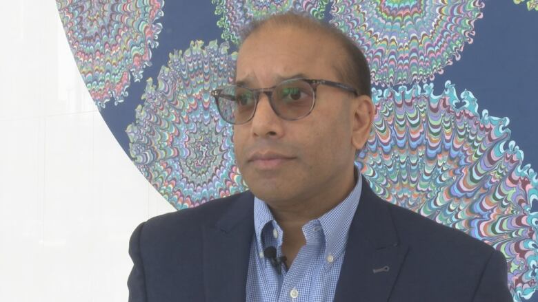 A man with glasses in front of a mural background