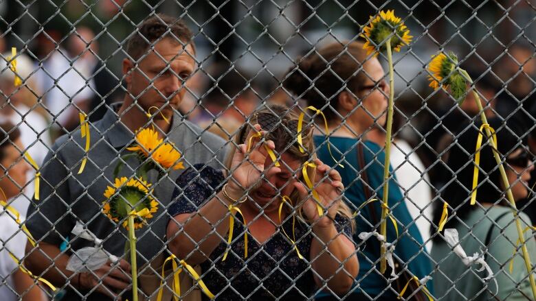 Mourners attach ribbons and flowers to a fence in Jimmie Simpson Park during a public vigil on Monday for Caroline Huebner-Makurat, after the mother of two was killed by a stray bullet in a daytime altercation in the city's east end on July 7. Cole Burston/CBC