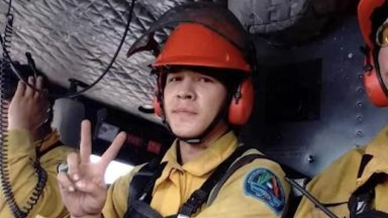 A young man in a helmet sitting inside an aircraft gives the peace sign.