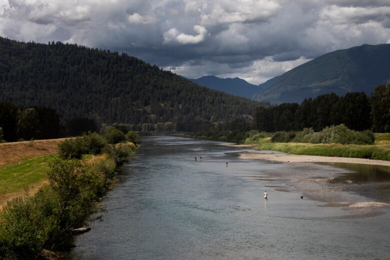 A wide shot of a river shows noticeably low water levels, with some fishermen able to wade to the centre of the river for their catch.