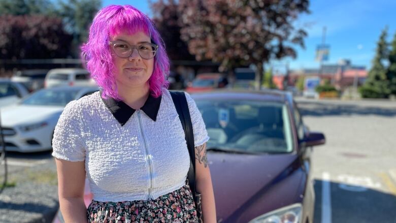 A pink-haired person smiles for a photo in a parking lot.