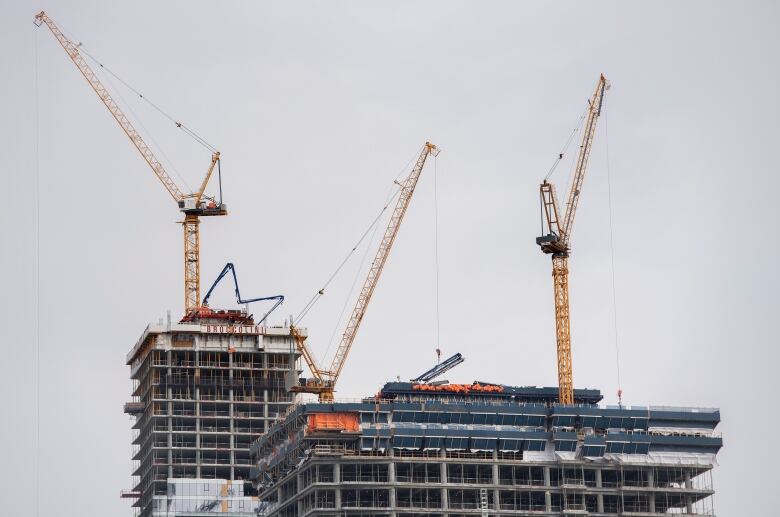 Three cranes dot the sky on under construction skyscrapers. 