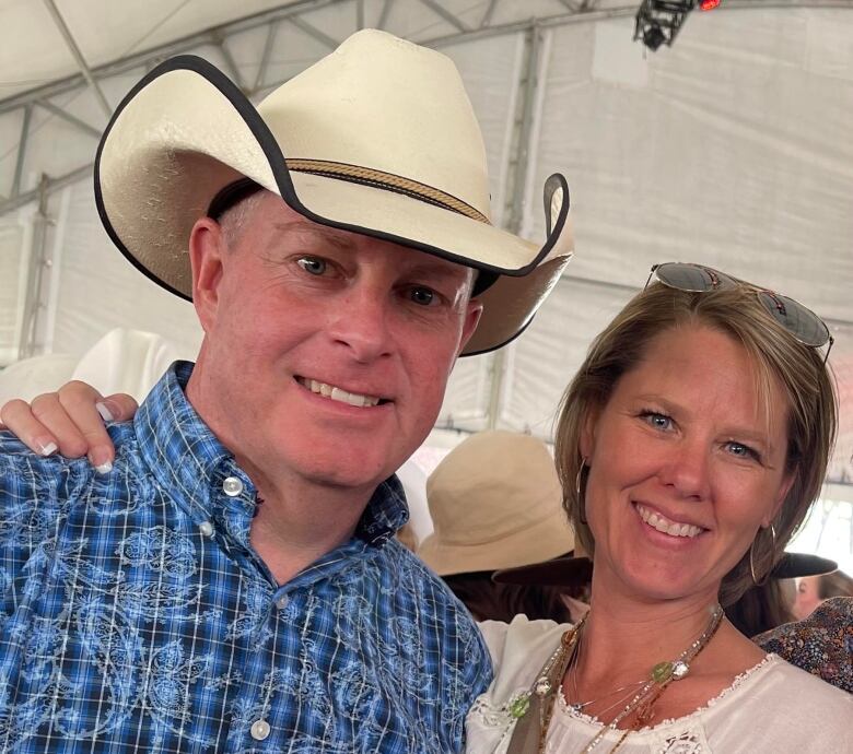 A man in a white hat and blue shirt next to a lady in white, are shown smiling in this photo.