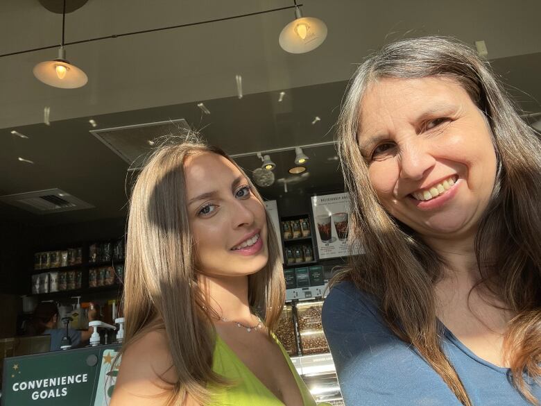 In a coffee shop, a young girl with a green tanktop and a woman in a blue shirt are smiling into the camera. 