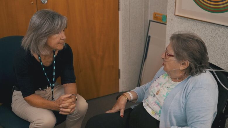 A woman is sitting down and talking to another woman. 