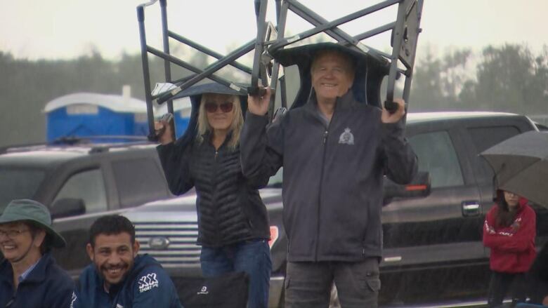 A man and a woman hold on to their chair to shelter from rain.