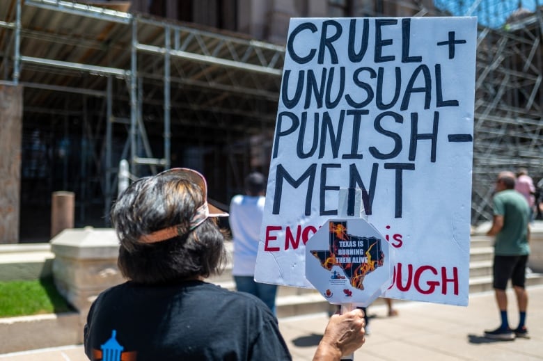 A person with their back turned holds a protest sign reading 