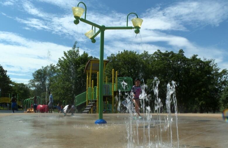 A splash pad in a playground with kids running through spraying water. 