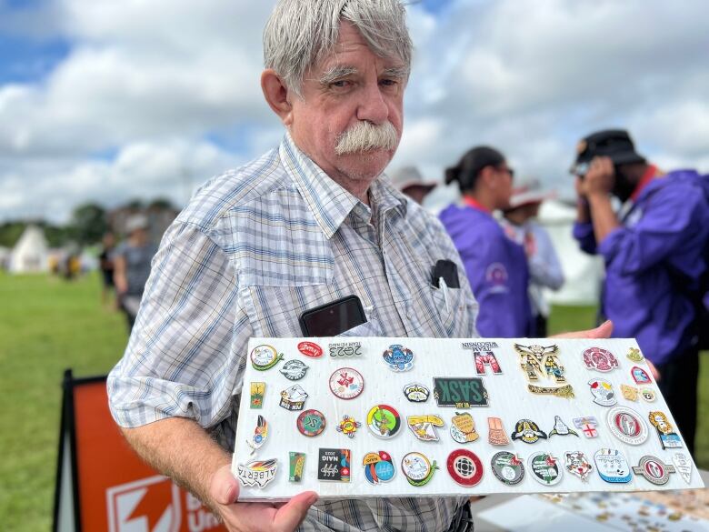 A man holds up a board of pins he's collected.