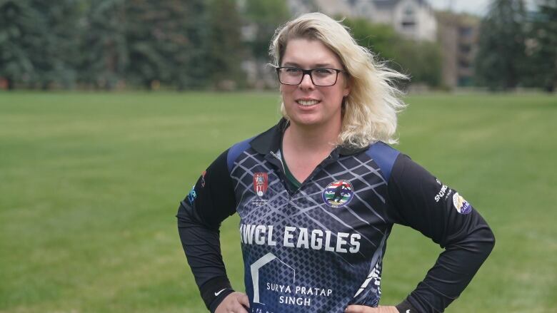 A lady with blonde hair and thick glasses is seen in a dark blue sports jersey.