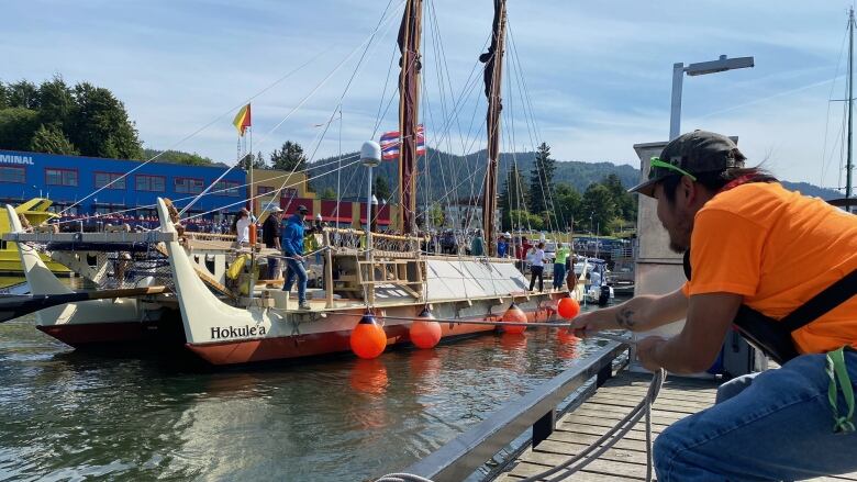 A man pulls a large, ornate canoe closer to the dock.