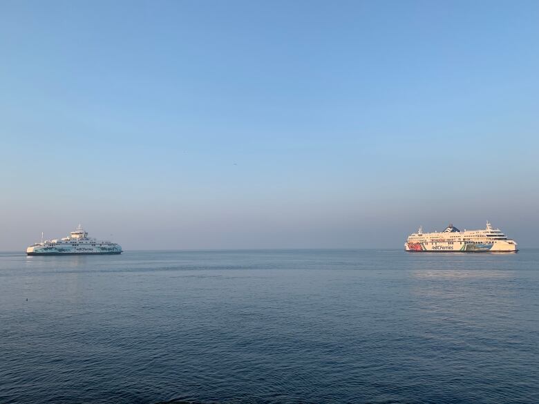 A large B.C. Ferry and a medium-sized ferry on open ocean with smoky summer sky. 