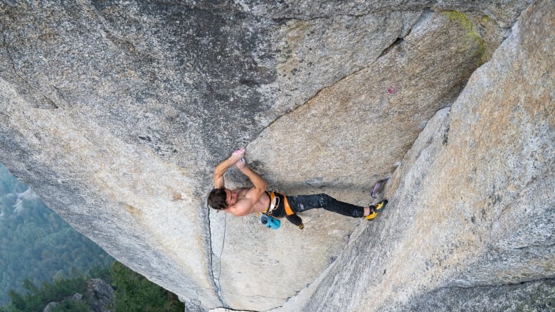 A shirtless man climbs up a very steep rockface hanging by a small crack. 