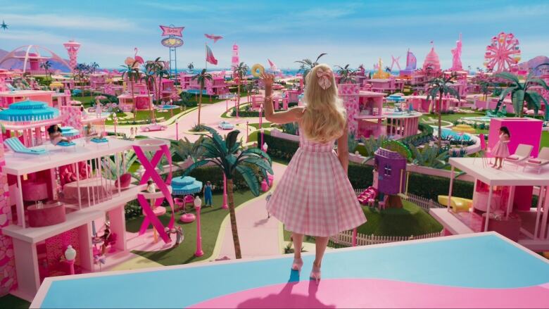 A wide shot of a woman standing on top of a building looking out into a vast pink city.