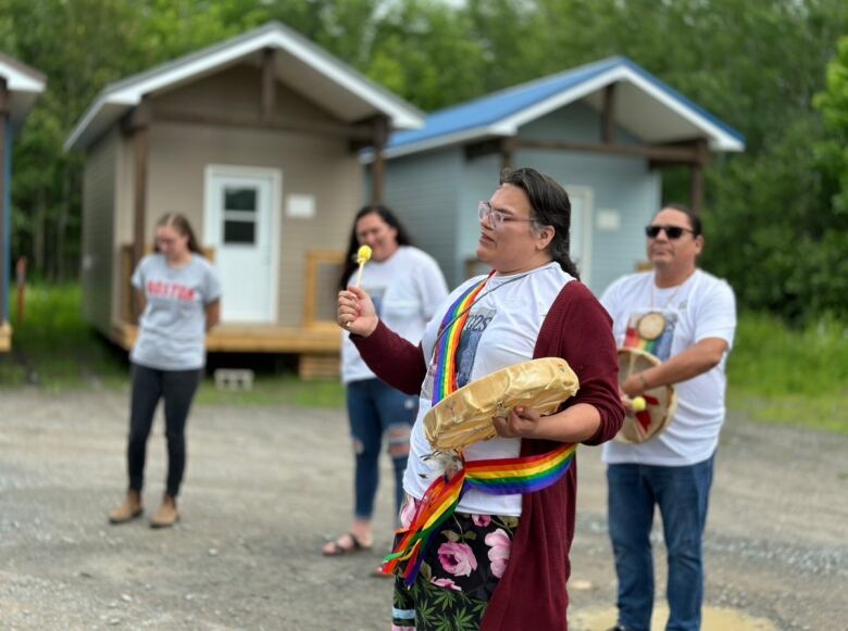 A person wearing a rainbow sash holds up a hand drum.