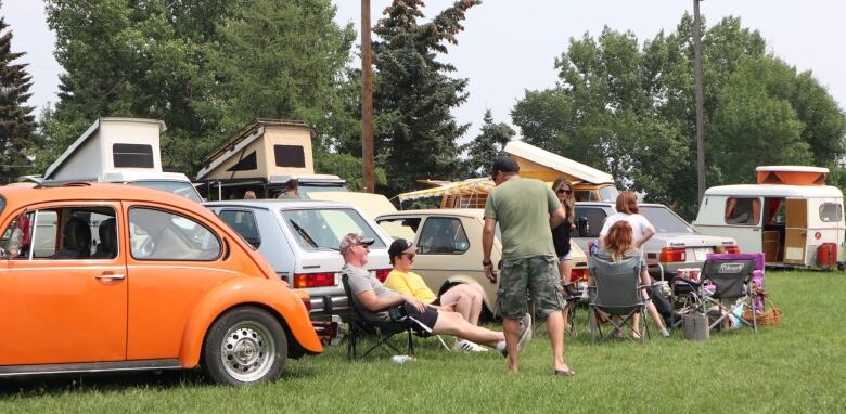 People sitting on lawn chairs and having a chat. They are sitting in front of some early model Volkswagen cars and campers. 