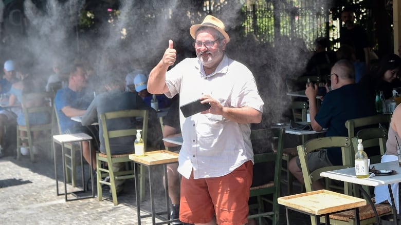 A tourist cools off under a mist of cool water in Athens, Greece.