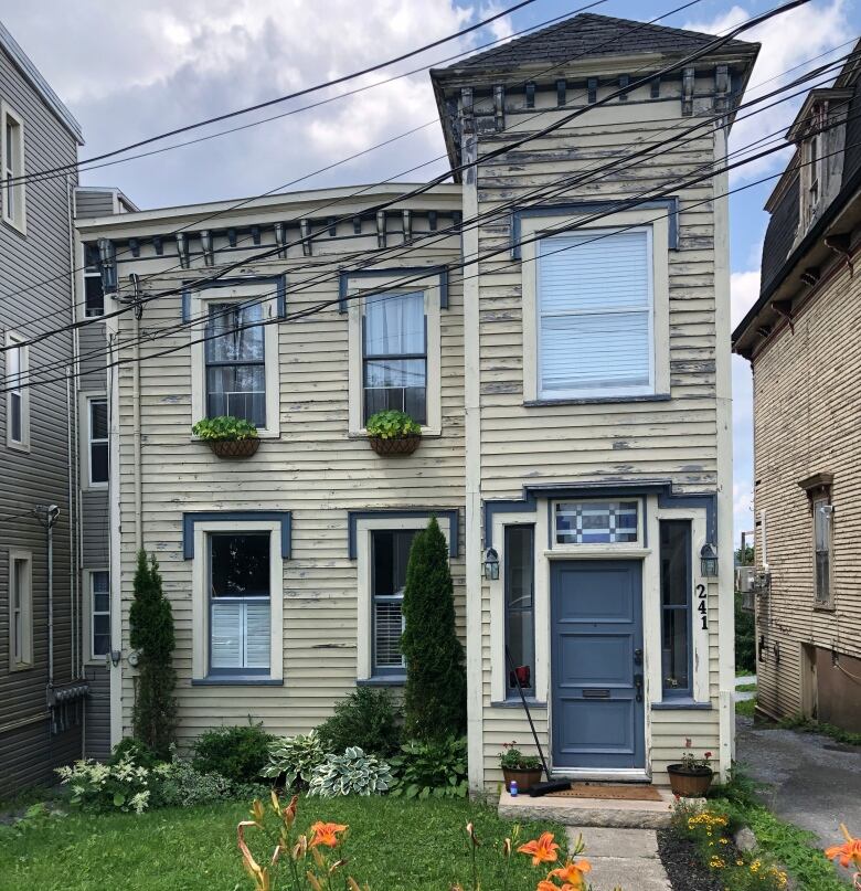 A narrow, 150-year-old house sits between two larger and taller ones along a city street. 