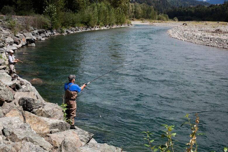 A fisherman with his line in the blue waters of a river bordered by a rocky shore on either side.