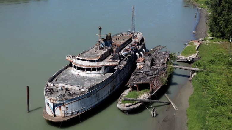 Two abandoned, dilapidated boats moored on a river.