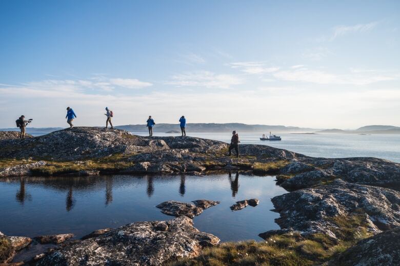 A group of six people are walking on a rocky hill with a large boat in the background. 