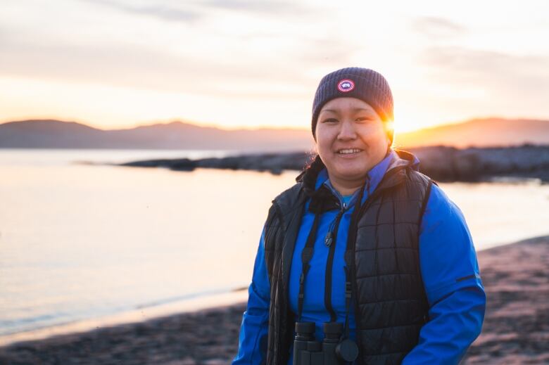 A young woman smiles with the sun setting behind her. 