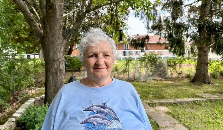 A woman stands in her backyard that has been damaged by a tornado.