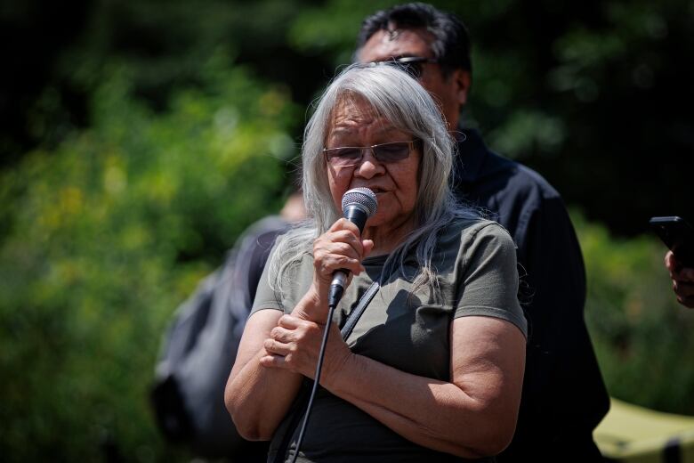 An older woman holds a microphone and speaks into it. 